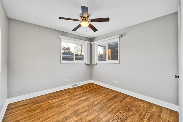 spare room with a ceiling fan, wood finished floors, visible vents, and baseboards