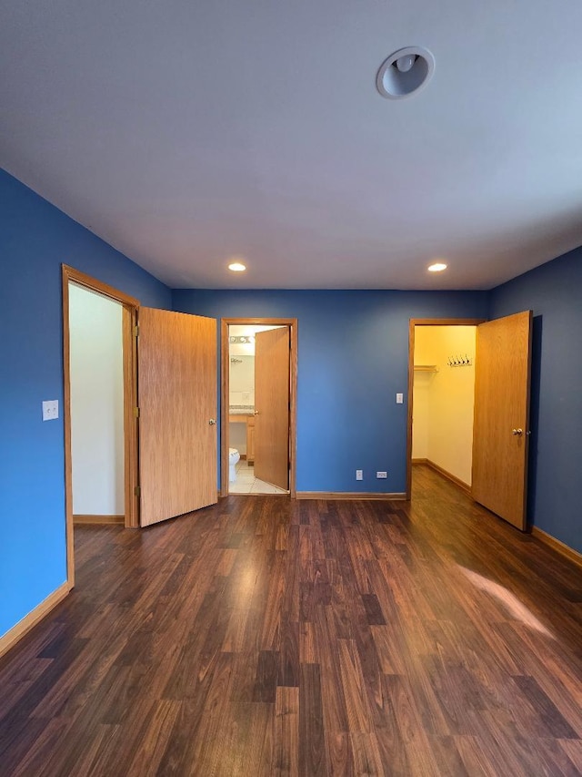 unfurnished bedroom featuring dark wood finished floors, ensuite bath, and baseboards