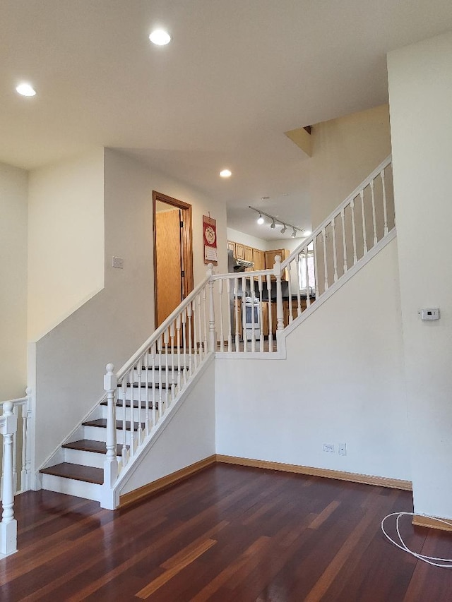 stairway featuring rail lighting, baseboards, wood finished floors, and recessed lighting