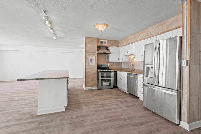 kitchen with light countertops, appliances with stainless steel finishes, white cabinetry, a sink, and wall chimney exhaust hood