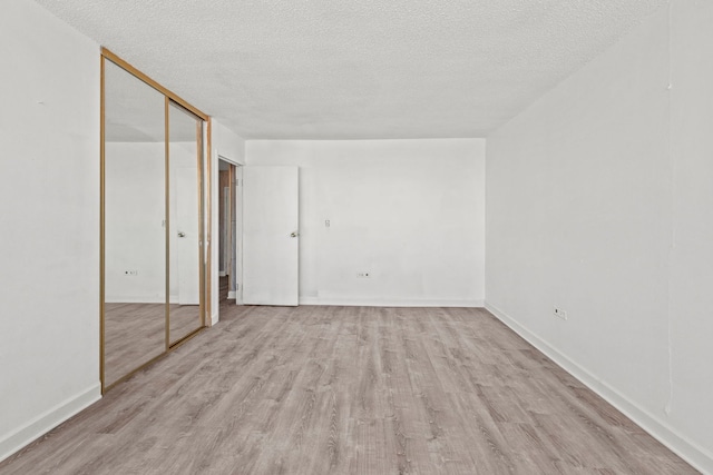 unfurnished bedroom with light wood-style floors, a closet, a textured ceiling, and baseboards