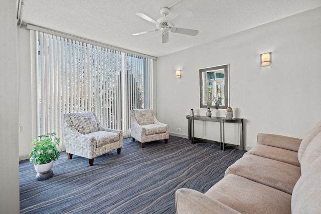 living area featuring baseboards, ceiling fan, a wall of windows, a textured ceiling, and dark colored carpet