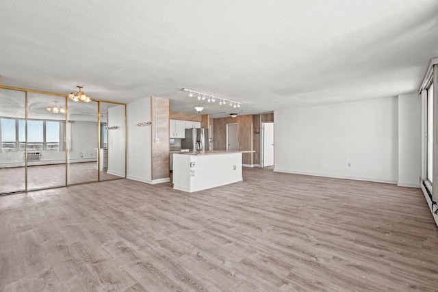 unfurnished living room featuring light wood-style floors, baseboards, a textured ceiling, and an inviting chandelier