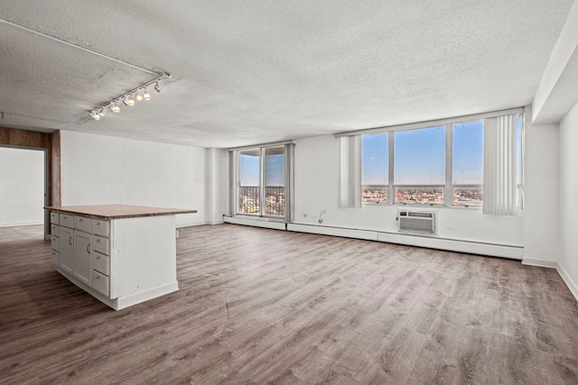 unfurnished living room with a textured ceiling, a baseboard radiator, baseboards, dark wood-style floors, and track lighting