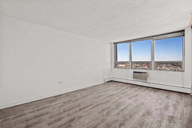 empty room with a textured ceiling, light wood finished floors, baseboard heating, and baseboards