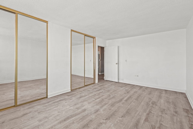 unfurnished bedroom with a textured ceiling, baseboards, two closets, and light wood-style floors