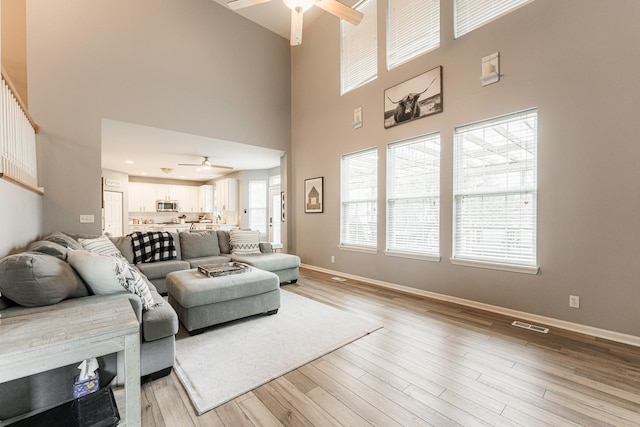 living room with light wood-style flooring, visible vents, baseboards, and a ceiling fan