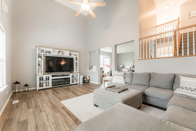 living area with ceiling fan, wood finished floors, a towering ceiling, and baseboards