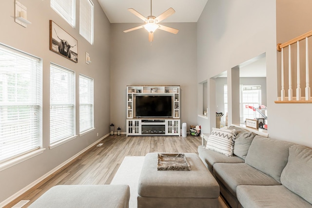 living area with light wood-type flooring, a high ceiling, baseboards, and a ceiling fan