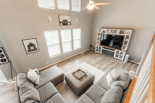 living room featuring a high ceiling, wood finished floors, a ceiling fan, and baseboards