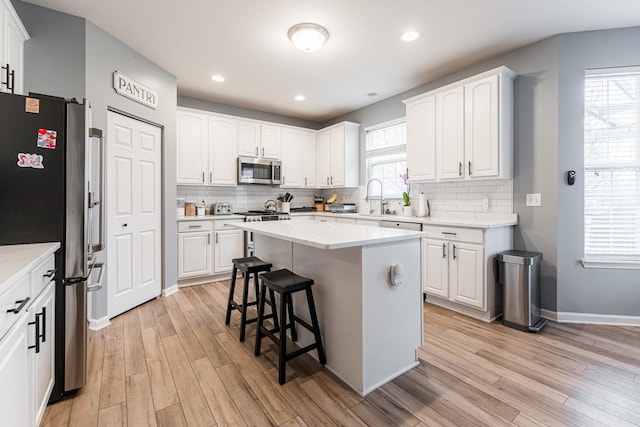 kitchen with stainless steel appliances, a breakfast bar, white cabinetry, and light wood-style flooring