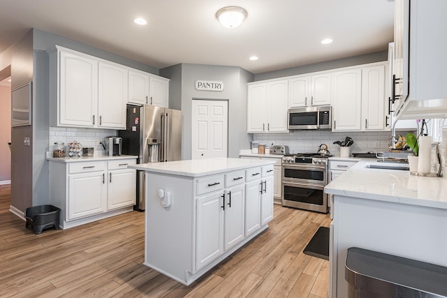 kitchen with light stone counters, light wood-style flooring, high quality appliances, and white cabinetry