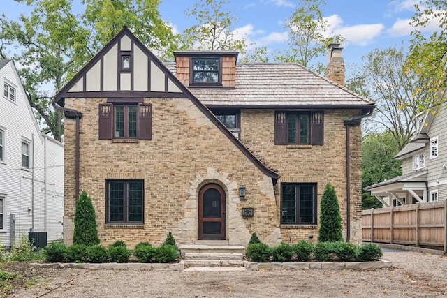 english style home featuring brick siding, a chimney, fence, and central air condition unit