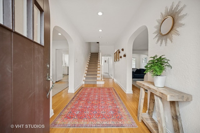 entrance foyer with light wood-style floors, stairs, baseboards, and arched walkways