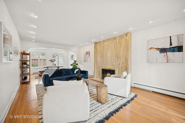 living area with a baseboard heating unit, a fireplace, wood finished floors, and recessed lighting