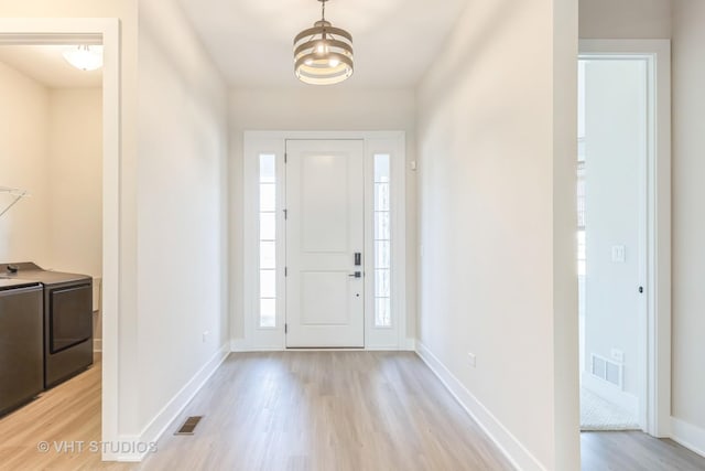 entryway with washer and clothes dryer, visible vents, light wood-style flooring, and baseboards