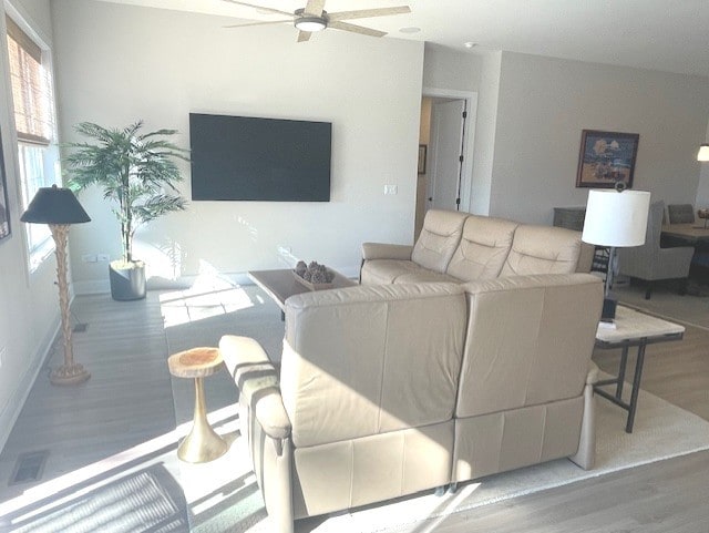 living area featuring a ceiling fan, baseboards, visible vents, and light wood finished floors