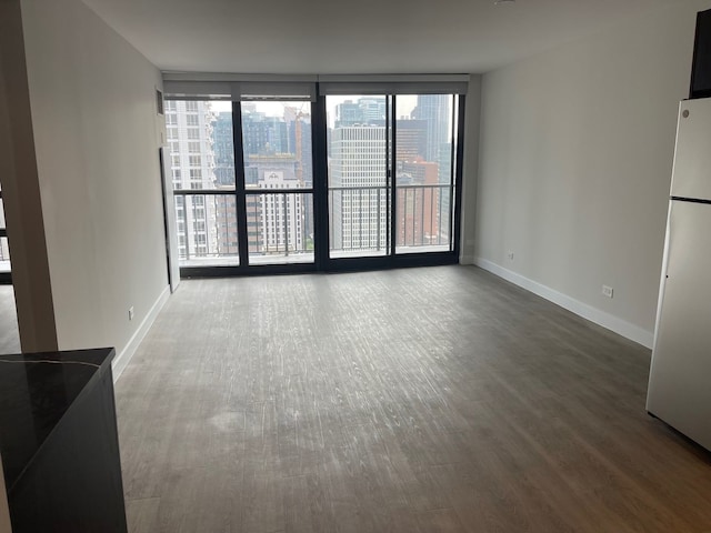 unfurnished living room with plenty of natural light, baseboards, wood finished floors, a view of city, and a wall of windows