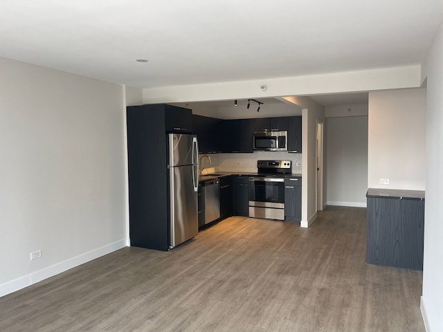 kitchen with light countertops, appliances with stainless steel finishes, wood finished floors, dark cabinets, and baseboards