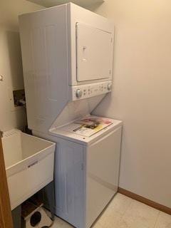 washroom featuring laundry area, stacked washer / dryer, a sink, and baseboards