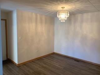 empty room featuring dark wood-style flooring, an inviting chandelier, and baseboards