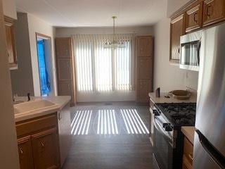 kitchen with pendant lighting, brown cabinets, stainless steel appliances, light countertops, and a sink