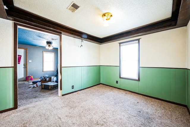 spare room with a textured ceiling, light carpet, wainscoting, and visible vents