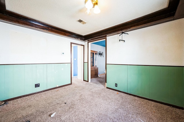 unfurnished room with light carpet, a textured ceiling, wainscoting, and visible vents