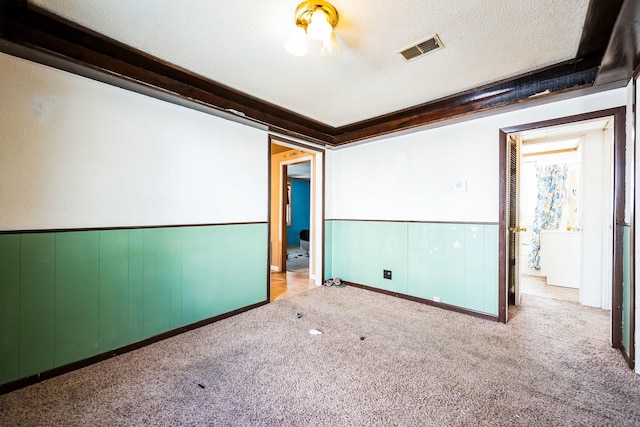 spare room with visible vents, wainscoting, light colored carpet, and a textured ceiling