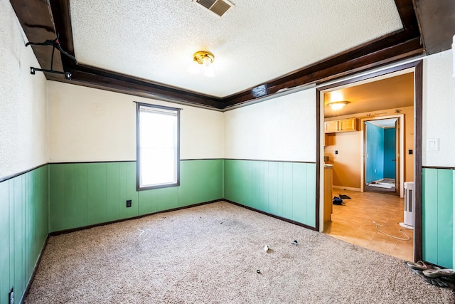 unfurnished room with visible vents, light colored carpet, a textured ceiling, and wainscoting