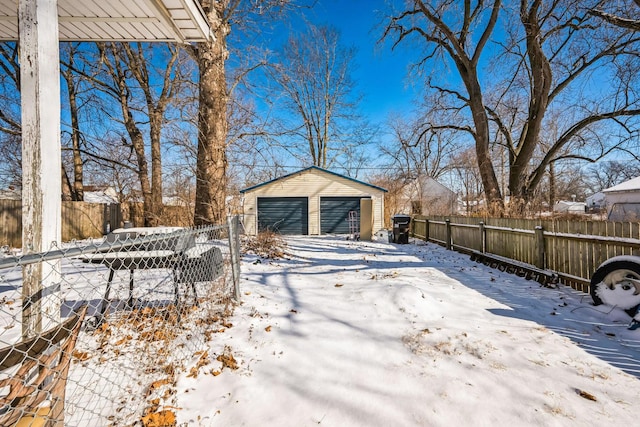 snowy yard with a detached garage, fence, and an outdoor structure