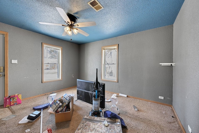 interior space with visible vents, a ceiling fan, a textured wall, a textured ceiling, and carpet floors