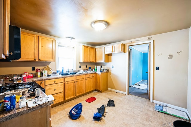 kitchen featuring gas cooktop, brown cabinets, a sink, and baseboards