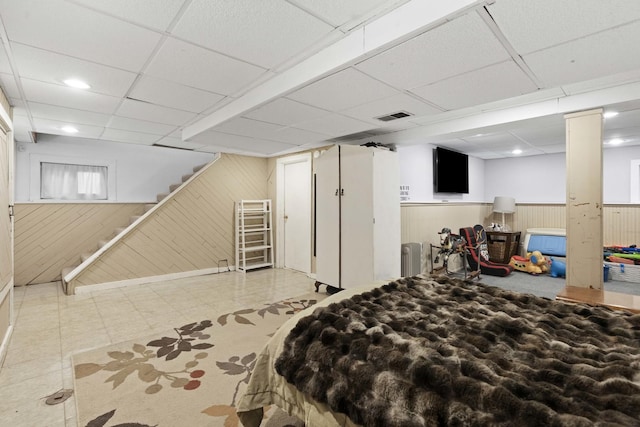 bedroom featuring a wainscoted wall, wooden walls, a paneled ceiling, and visible vents