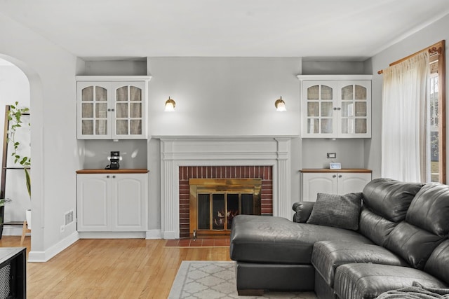 living area featuring light wood finished floors, visible vents, a brick fireplace, baseboards, and arched walkways