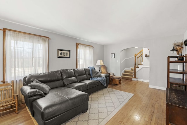 living area with arched walkways, light wood-style flooring, stairs, and baseboards