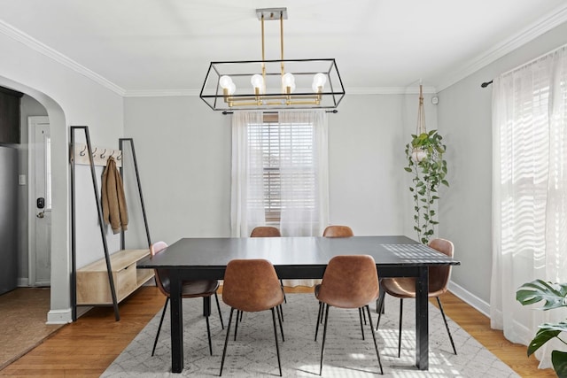 dining room featuring light wood-type flooring, arched walkways, ornamental molding, and a chandelier