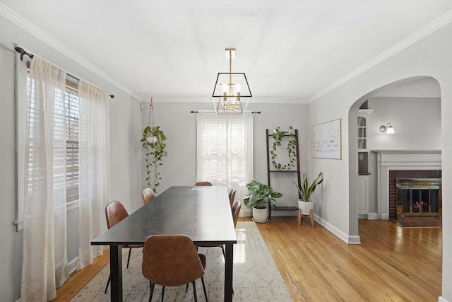 dining area with arched walkways, light wood-style floors, a chandelier, and crown molding