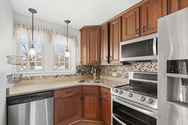 kitchen with a sink, light stone counters, tasteful backsplash, stainless steel appliances, and hanging light fixtures