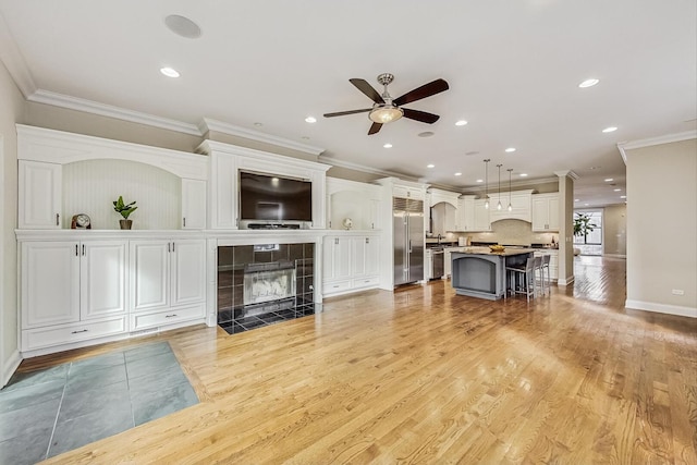 living area with ornamental molding, recessed lighting, light wood-style flooring, a tile fireplace, and a ceiling fan