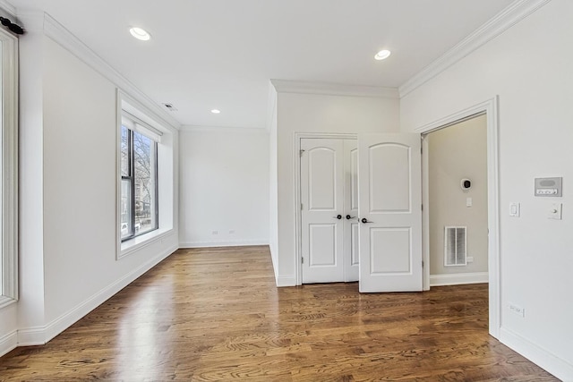 interior space featuring visible vents, wood finished floors, baseboards, and ornamental molding