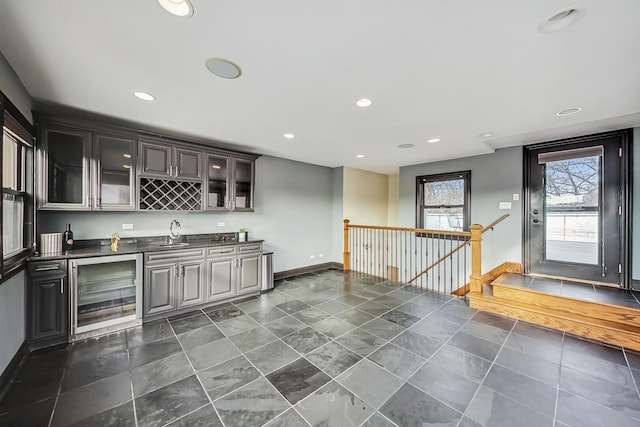 bar featuring baseboards, wine cooler, recessed lighting, wet bar, and a sink