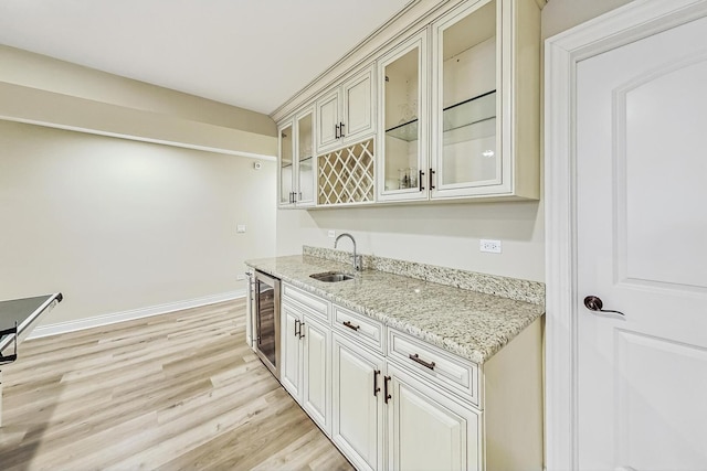 kitchen featuring a sink, wine cooler, light wood finished floors, glass insert cabinets, and light stone countertops