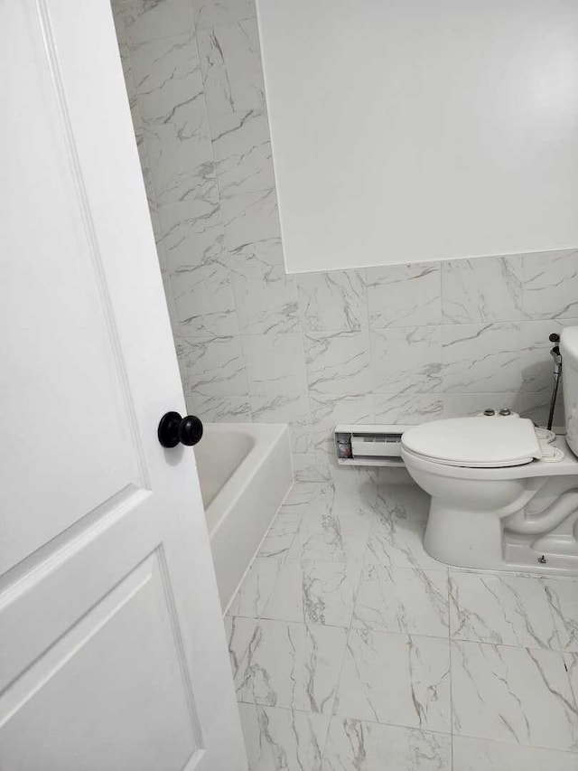 full bathroom featuring tile walls, toilet, marble finish floor, and a washtub