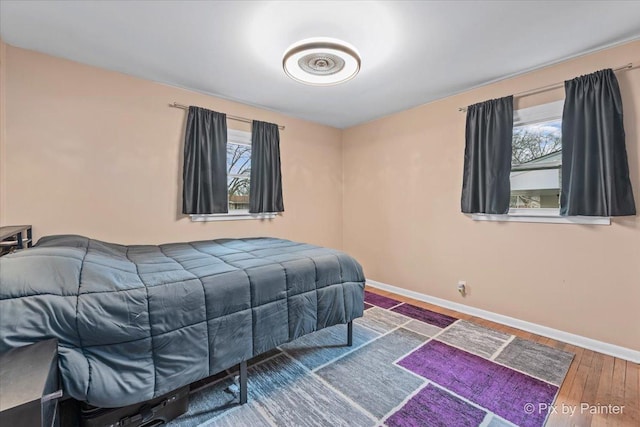 bedroom with multiple windows, wood finished floors, and baseboards