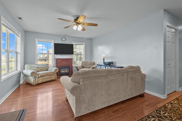 living area with visible vents, baseboards, a ceiling fan, a glass covered fireplace, and wood finished floors