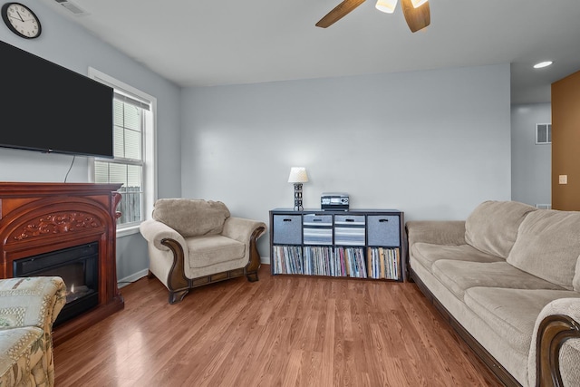 living area with light wood-style floors, a glass covered fireplace, visible vents, and a ceiling fan