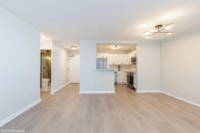 unfurnished living room with light wood-style flooring, baseboards, and an inviting chandelier