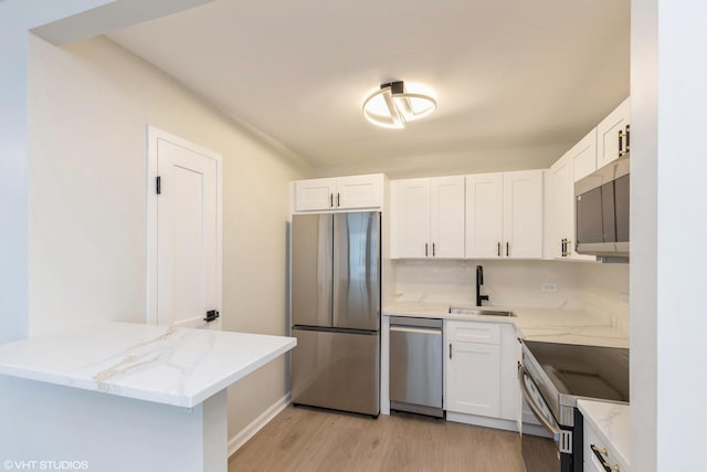 kitchen with light stone countertops, appliances with stainless steel finishes, white cabinets, and a sink