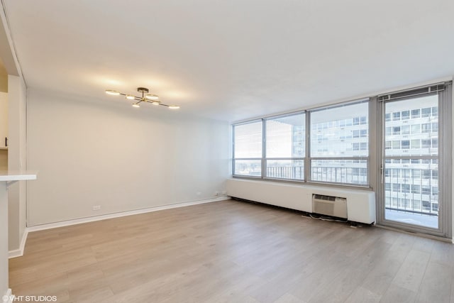 unfurnished room with light wood-style flooring, baseboards, and a wall mounted air conditioner